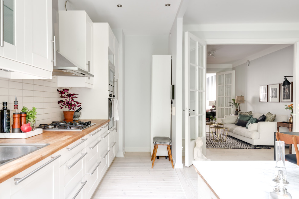 Geschlossene Skandinavische Küche mit Schrankfronten mit vertiefter Füllung, weißen Schränken, Arbeitsplatte aus Holz und Kücheninsel in Stockholm