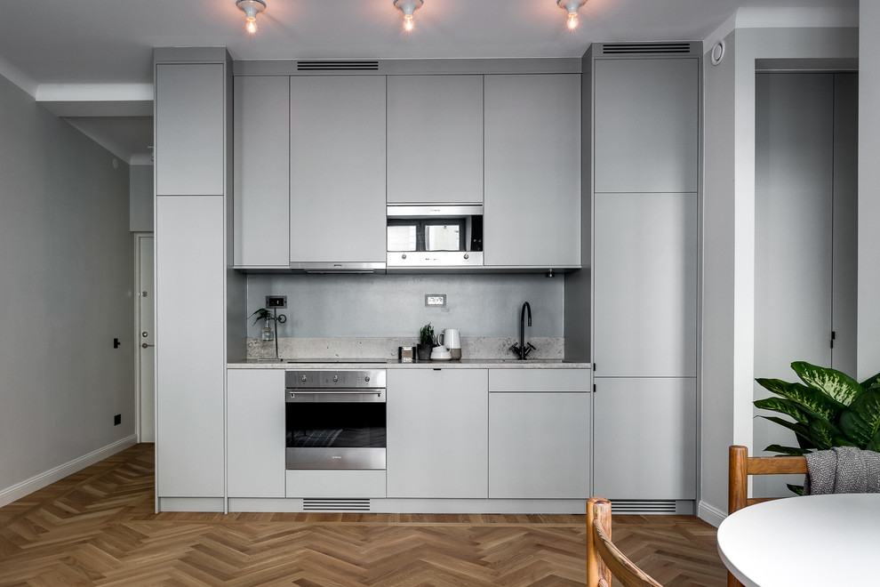Photo of a medium sized scandi single-wall kitchen/diner in Stockholm with flat-panel cabinets, grey cabinets, grey splashback, stainless steel appliances, light hardwood flooring and no island.