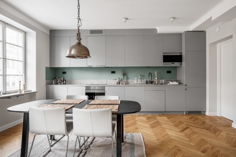 Foto de cocina comedor lineal escandinava de tamaño medio sin isla con armarios con paneles lisos, puertas de armario grises, salpicadero gris, electrodomésticos de acero inoxidable, suelo de madera en tonos medios y encimera de mármol