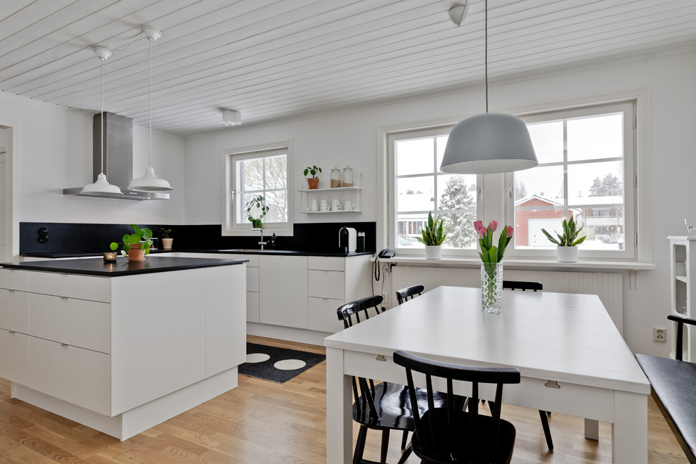 Aménagement d'une grande cuisine ouverte scandinave avec un placard à porte plane, des portes de placard blanches, un plan de travail en granite, un sol en bois brun, îlot et un sol marron.