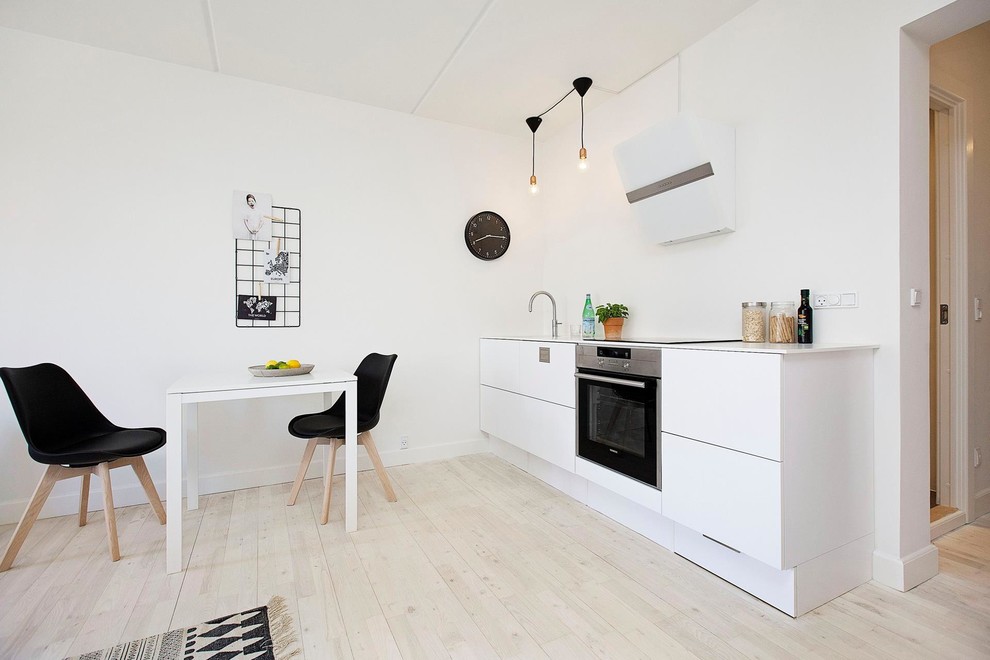 Photo of a medium sized scandi single-wall kitchen/diner in Copenhagen with a single-bowl sink, flat-panel cabinets, white cabinets, laminate countertops, stainless steel appliances, light hardwood flooring and no island.