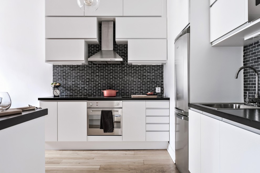 Ejemplo de cocina lineal actual con armarios con paneles lisos, salpicadero negro, salpicadero de ladrillos, electrodomésticos de acero inoxidable y con blanco y negro