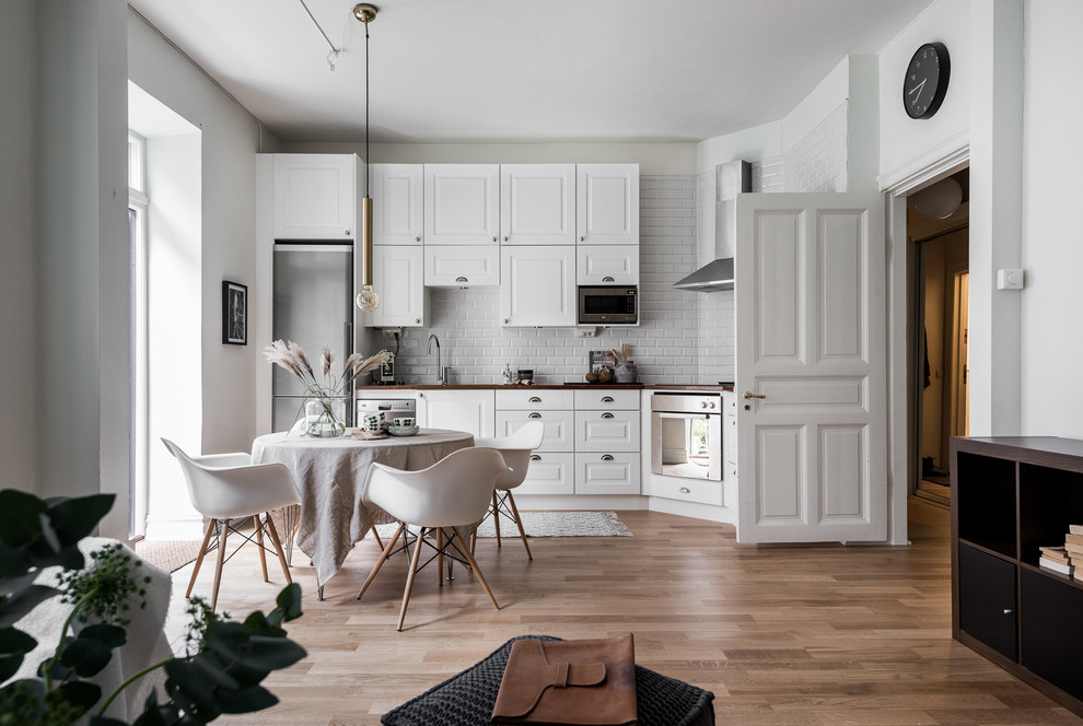 Einzeilige, Mittelgroße Skandinavische Küche ohne Insel mit Schrankfronten im Shaker-Stil, weißen Schränken, Küchengeräten aus Edelstahl und braunem Holzboden in Göteborg