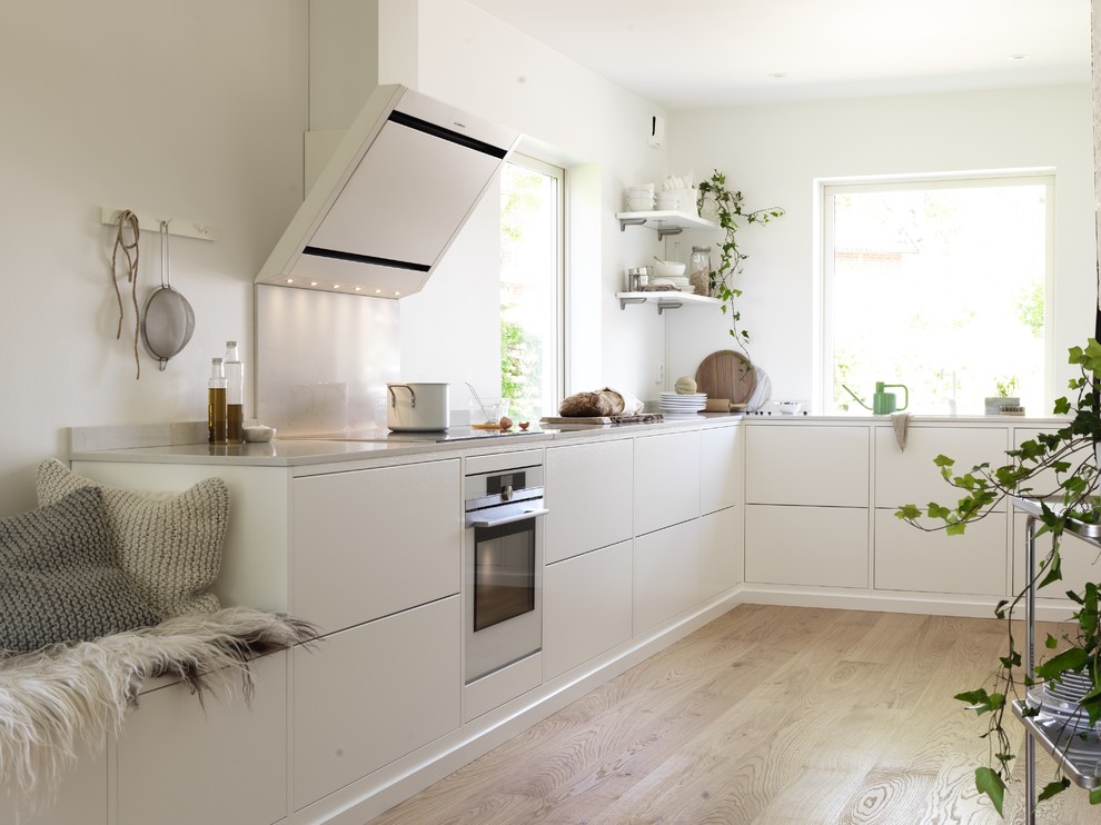 Large contemporary l-shaped kitchen in Malmo with flat-panel cabinets, white cabinets, stainless steel appliances, light hardwood flooring and no island.