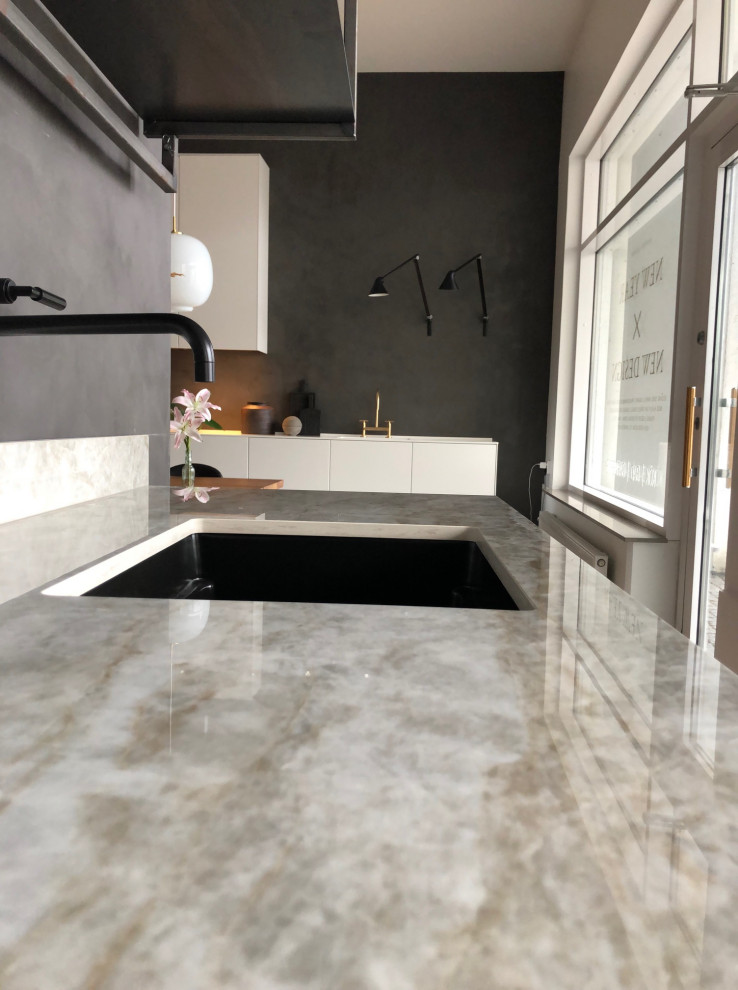 Foto på ett mellanstort nordiskt beige linjärt kök och matrum, med en enkel diskho, släta luckor, svarta skåp, bänkskiva i kvarts, beige stänkskydd, svarta vitvaror, betonggolv och grått golv