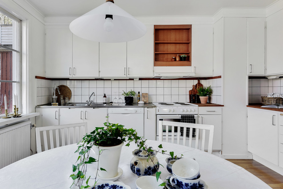 ストックホルムにある北欧スタイルのおしゃれなキッチン (一体型シンク、フラットパネル扉のキャビネット、白いキャビネット、木材カウンター、白いキッチンパネル、白い調理設備、無垢フローリング、アイランドなし、茶色い床、茶色いキッチンカウンター) の写真