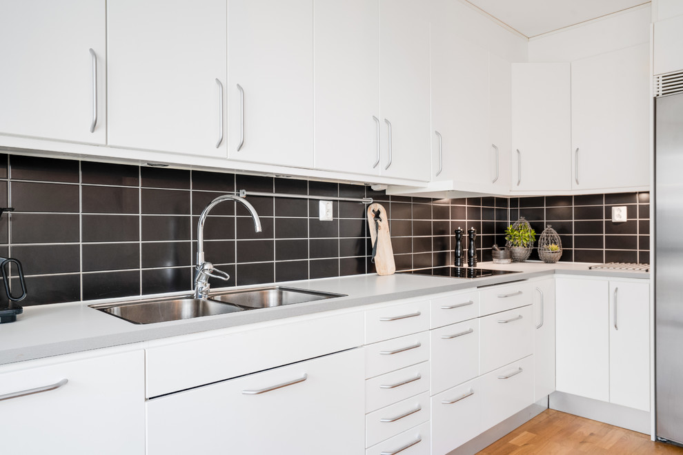 Bild på ett mellanstort funkis kök, med släta luckor, vita skåp, laminatbänkskiva, svart stänkskydd och rostfria vitvaror