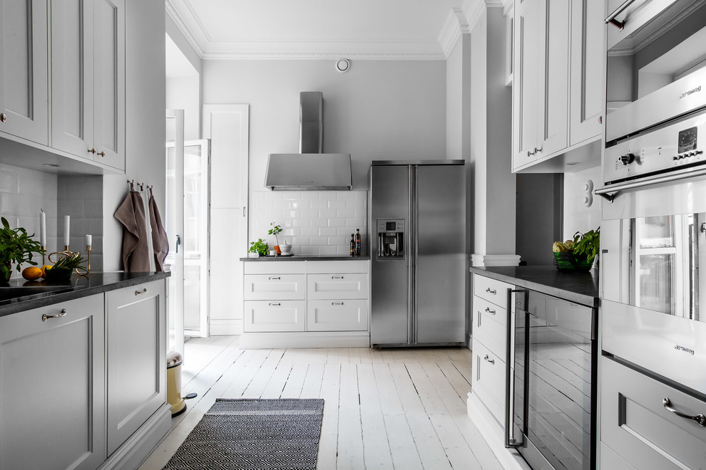 Imagen de cocina clásica sin isla con electrodomésticos de acero inoxidable, suelo de madera pintada, suelo blanco y armarios con paneles empotrados