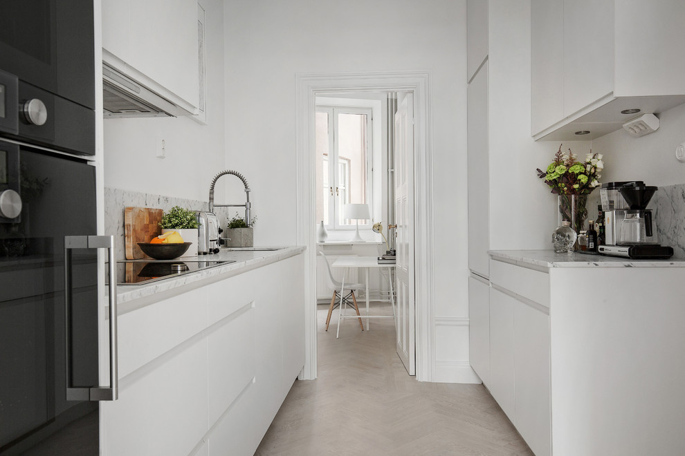 Стильный дизайн: параллельная кухня среднего размера в скандинавском стиле с врезной мойкой, плоскими фасадами, черной техникой, светлым паркетным полом, мраморной столешницей и черно-белыми фасадами без острова - последний тренд