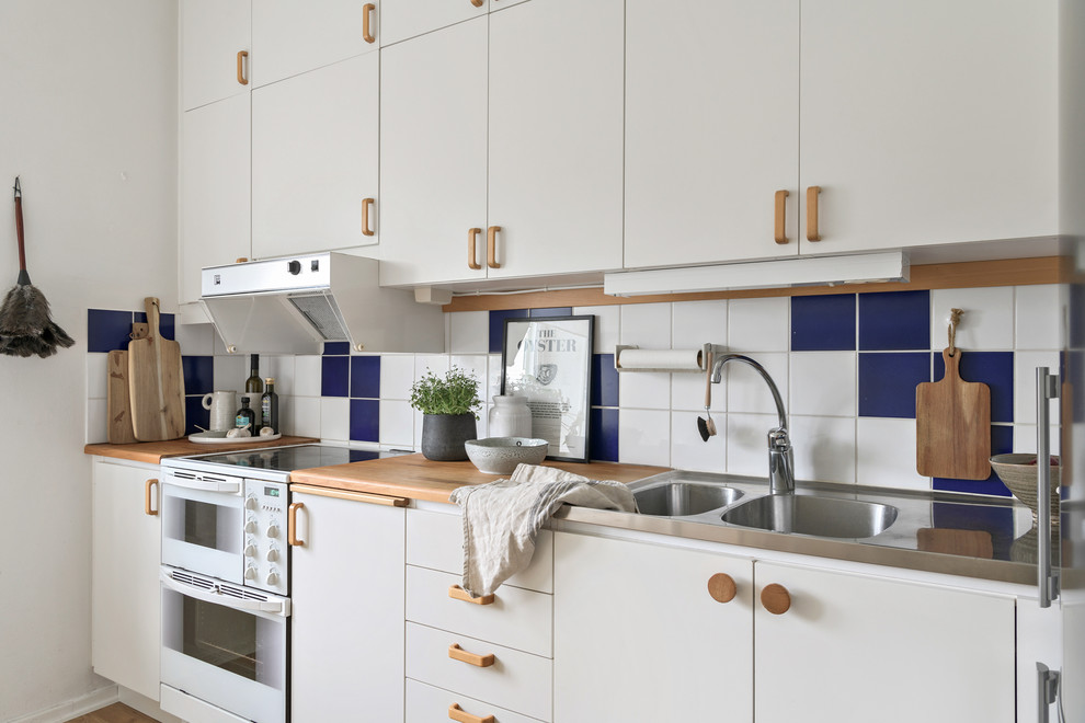 Inspiration för ett minimalistiskt linjärt kök, med en dubbel diskho, släta luckor, vita skåp, träbänkskiva, flerfärgad stänkskydd och vita vitvaror