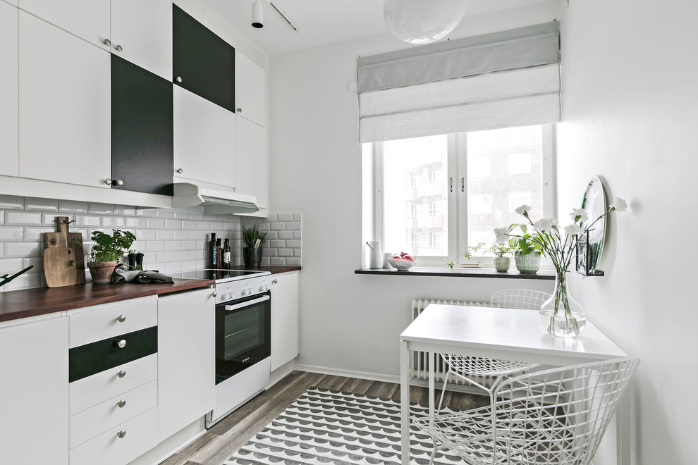 Bild på ett litet minimalistiskt linjärt kök och matrum, med släta luckor, vita vitvaror, brunt golv, vita skåp, vitt stänkskydd, stänkskydd i tunnelbanekakel och mörkt trägolv