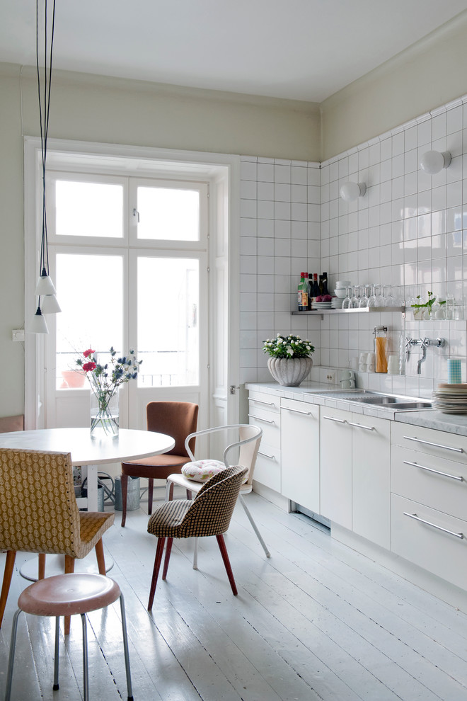 Foto på ett mellanstort skandinaviskt linjärt kök och matrum, med en dubbel diskho, släta luckor, vita skåp, bänkskiva i rostfritt stål, vita vitvaror och målat trägolv