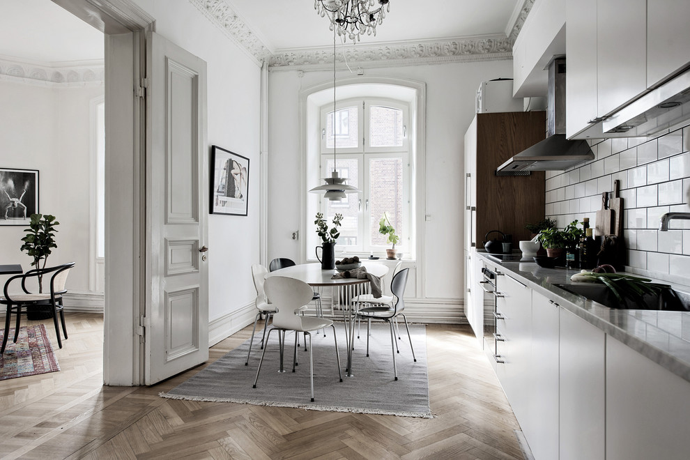 Foto på ett stort nordiskt linjärt kök och matrum, med en enkel diskho, släta luckor, vita skåp, vitt stänkskydd, stänkskydd i tunnelbanekakel, integrerade vitvaror, mellanmörkt trägolv och brunt golv