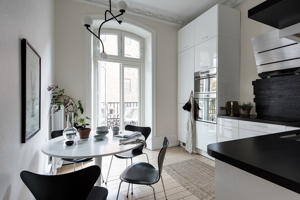Idéer för skandinaviska svart kök, med en undermonterad diskho, släta luckor, vita skåp, svart stänkskydd, stänkskydd i stickkakel, rostfria vitvaror, ljust trägolv och beiget golv