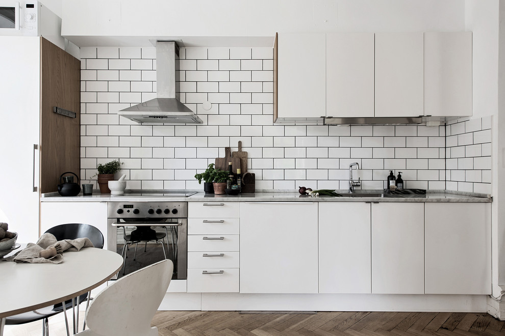 Exempel på ett minimalistiskt linjärt kök och matrum, med släta luckor, vita skåp, vitt stänkskydd, stänkskydd i tunnelbanekakel, integrerade vitvaror, mellanmörkt trägolv och brunt golv