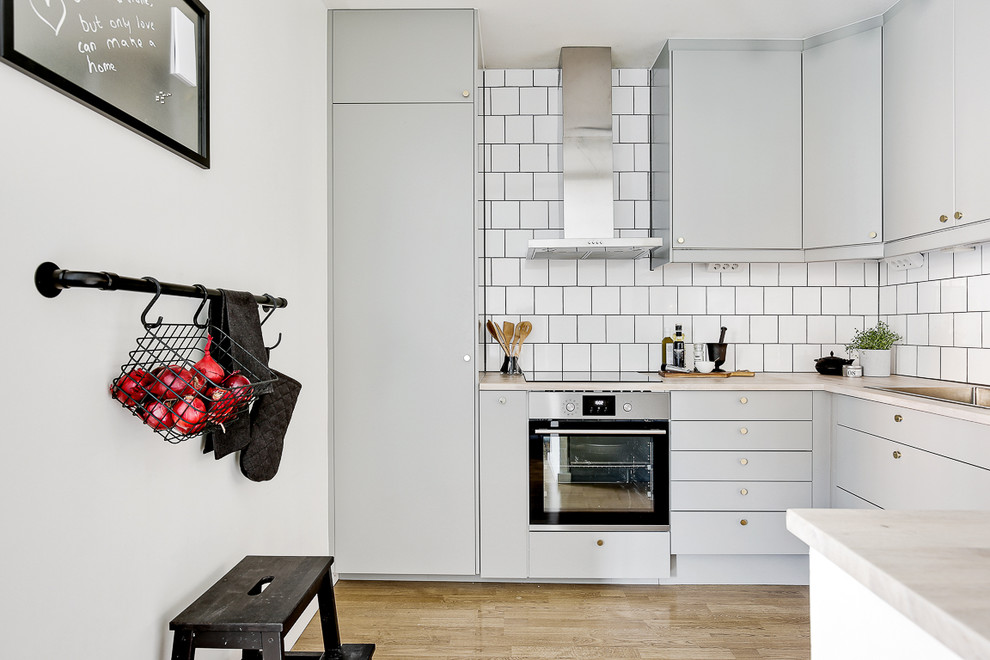 Nordische Küche in U-Form mit flächenbündigen Schrankfronten, grauen Schränken, Küchenrückwand in Weiß, Küchengeräten aus Edelstahl, hellem Holzboden und beigem Boden in Stockholm
