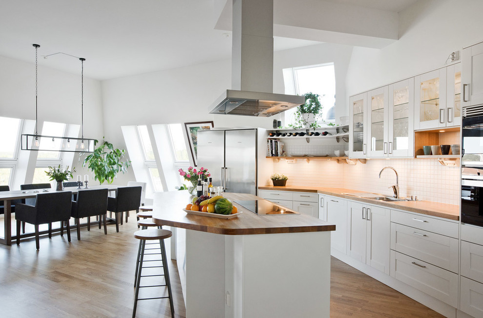 Inspiration för ett skandinaviskt linjärt kök, med en dubbel diskho, luckor med glaspanel, vita skåp, träbänkskiva, vitt stänkskydd, rostfria vitvaror, ljust trägolv och en köksö