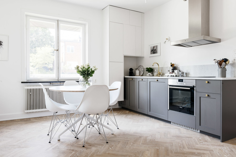 Inredning av ett skandinaviskt mellanstort linjärt kök och matrum, med luckor med infälld panel, grå skåp, marmorbänkskiva och ljust trägolv