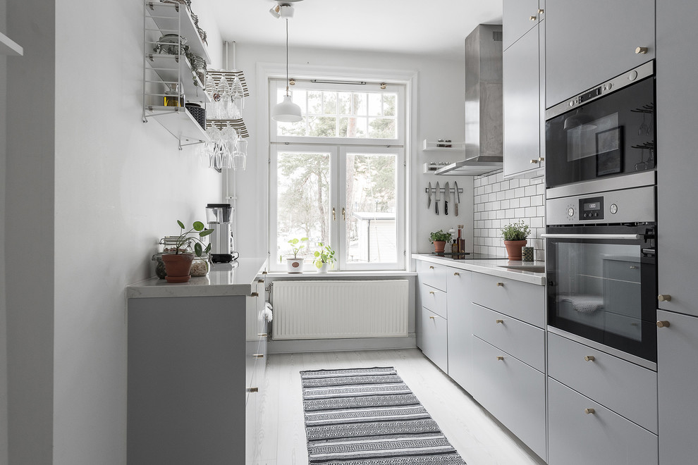 ストックホルムにある北欧スタイルのおしゃれなI型キッチン (アンダーカウンターシンク、フラットパネル扉のキャビネット、グレーのキャビネット、白いキッチンパネル、サブウェイタイルのキッチンパネル、白い床、白いキッチンカウンター) の写真