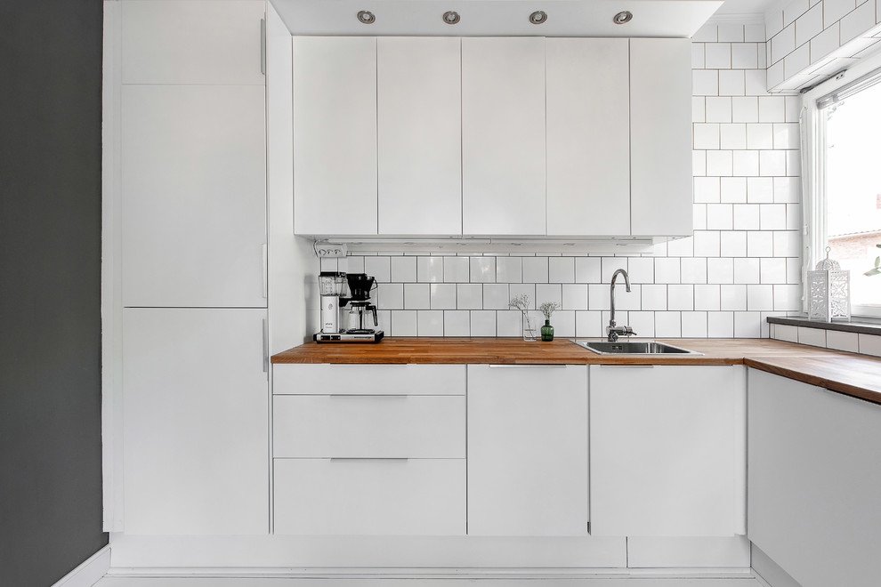 Foto på ett avskilt, litet skandinaviskt l-kök, med släta luckor, vita skåp, träbänkskiva och vitt stänkskydd