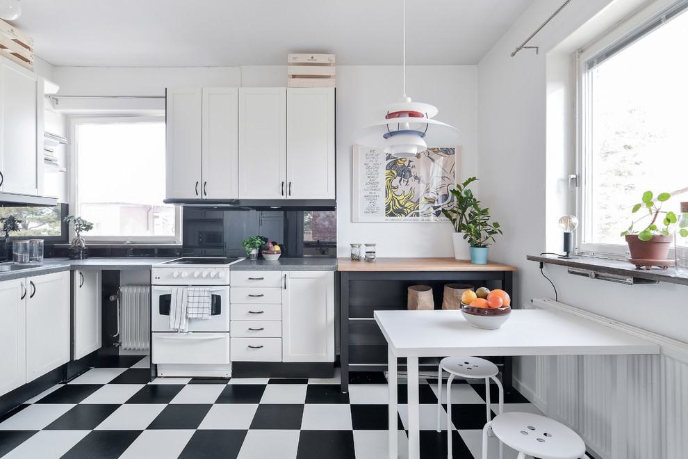 Nordische Wohnküche in L-Form mit Schrankfronten im Shaker-Stil, weißen Schränken, Küchenrückwand in Schwarz, Glasrückwand, weißen Elektrogeräten, buntem Boden und grauer Arbeitsplatte in Stockholm