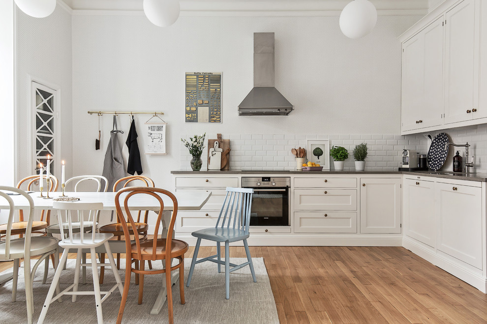 This is an example of a medium sized scandi l-shaped kitchen/diner in Stockholm with a single-bowl sink, raised-panel cabinets, white cabinets, concrete worktops, stainless steel appliances, medium hardwood flooring and no island.