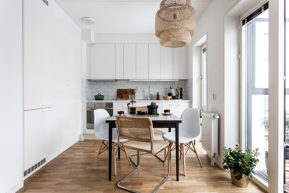 Idées déco pour une cuisine américaine linéaire scandinave de taille moyenne avec un placard à porte plane, des portes de placard blanches, une crédence blanche, une crédence en carrelage métro, un électroménager en acier inoxydable, parquet clair et aucun îlot.