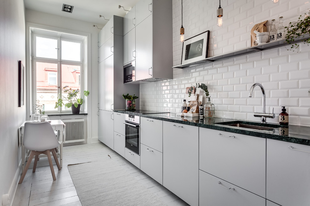 Idéer för att renovera ett stort minimalistiskt linjärt kök och matrum, med en undermonterad diskho, släta luckor, grå skåp, vitt stänkskydd, stänkskydd i tunnelbanekakel, svarta vitvaror och målat trägolv