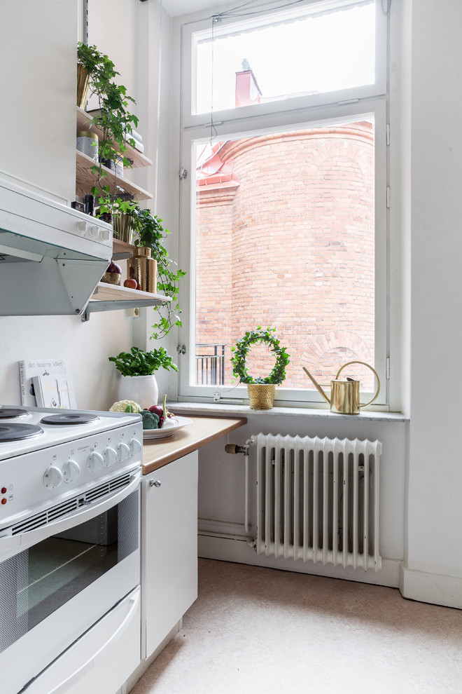 Nordisk inredning av ett avskilt, mellanstort linjärt kök, med släta luckor, vita skåp, träbänkskiva, vita vitvaror och linoleumgolv