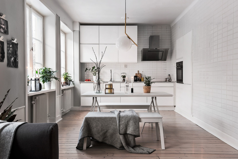 Cette photo montre une petite cuisine ouverte scandinave avec un placard à porte plane, des portes de placard blanches, une crédence blanche, parquet foncé et un électroménager noir.