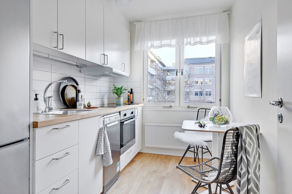 Bild på ett minimalistiskt linjärt kök och matrum, med en nedsänkt diskho, släta luckor, vita skåp, vitt stänkskydd, rostfria vitvaror och ljust trägolv