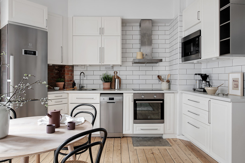 Nordisk inredning av ett vit vitt kök och matrum, med en enkel diskho, luckor med upphöjd panel, vita skåp, vitt stänkskydd, stänkskydd i tunnelbanekakel, rostfria vitvaror, ljust trägolv och beiget golv
