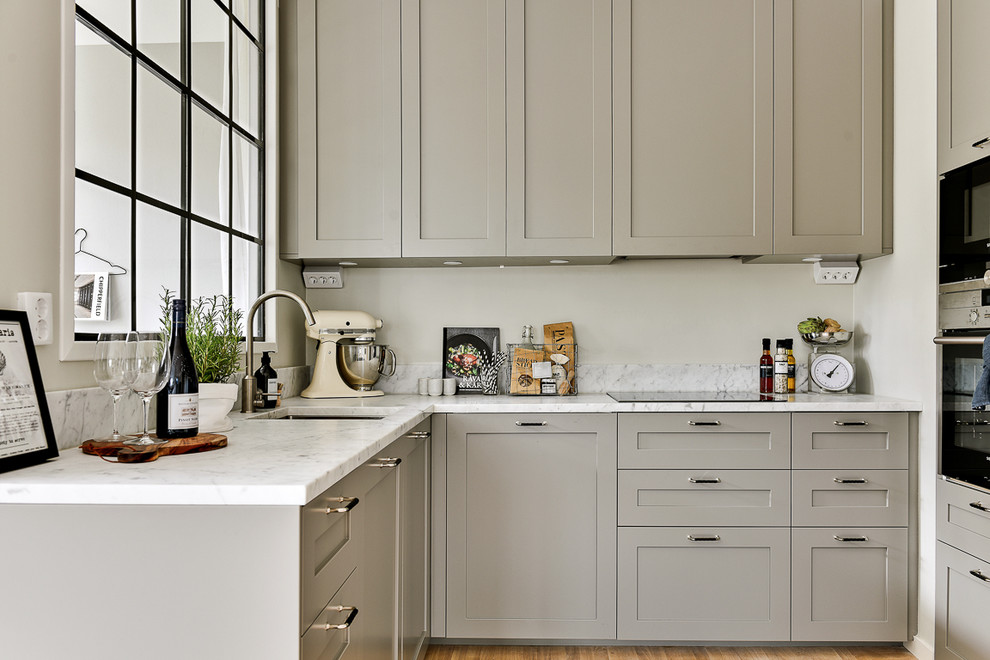 Bild på ett mellanstort minimalistiskt linjärt kök, med luckor med infälld panel, grå skåp, marmorbänkskiva, rostfria vitvaror och ljust trägolv