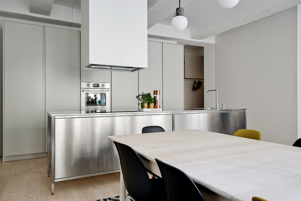 Modern inredning av ett mellanstort linjärt kök och matrum, med släta luckor, grå skåp, en köksö, rostfria vitvaror och ljust trägolv