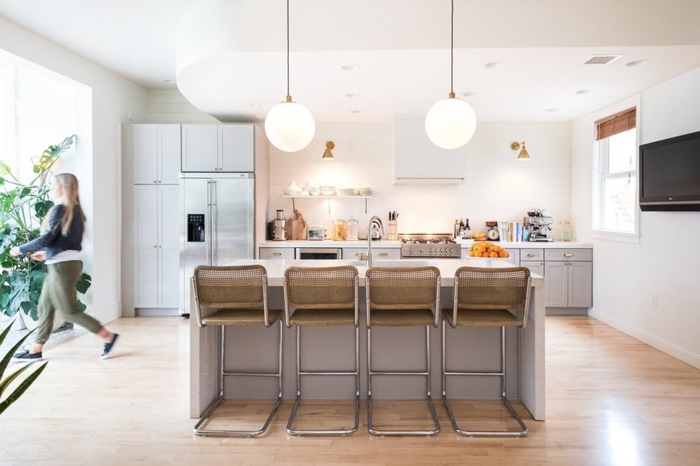 This is an example of a medium sized classic single-wall kitchen in Stockholm with shaker cabinets, grey cabinets, white splashback, stainless steel appliances, light hardwood flooring and an island.