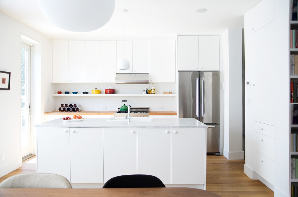 Modelo de cocina comedor contemporánea grande con armarios con paneles lisos, puertas de armario blancas, electrodomésticos de acero inoxidable, suelo de madera en tonos medios, una isla, fregadero de un seno y encimera de mármol