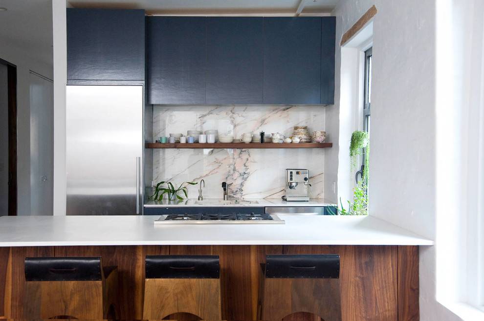 Cette photo montre une cuisine linéaire moderne en bois brun de taille moyenne avec un placard sans porte, une crédence blanche, un électroménager en acier inoxydable, une péninsule, un évier posé et plan de travail en marbre.