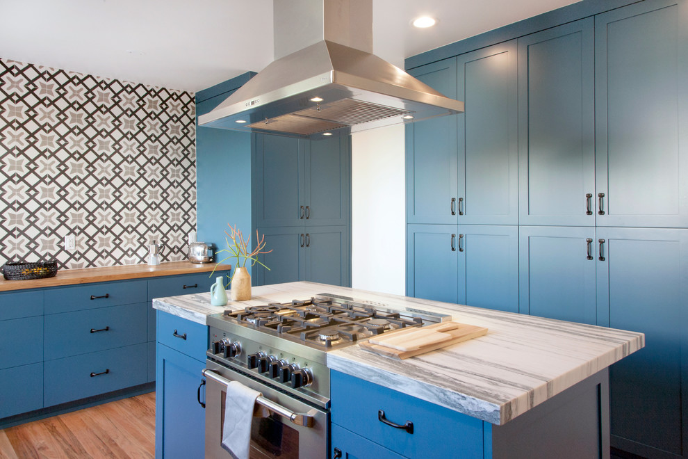 Idee per una cucina chic di medie dimensioni con ante in stile shaker, ante blu, paraspruzzi multicolore, elettrodomestici in acciaio inossidabile, parquet chiaro e top in legno
