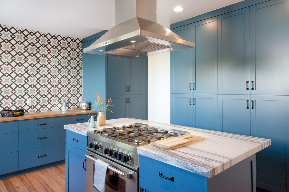Inspiration for a mid-sized transitional single-wall light wood floor kitchen remodel in Stockholm with shaker cabinets, blue cabinets, multicolored backsplash, stainless steel appliances, an island and wood countertops