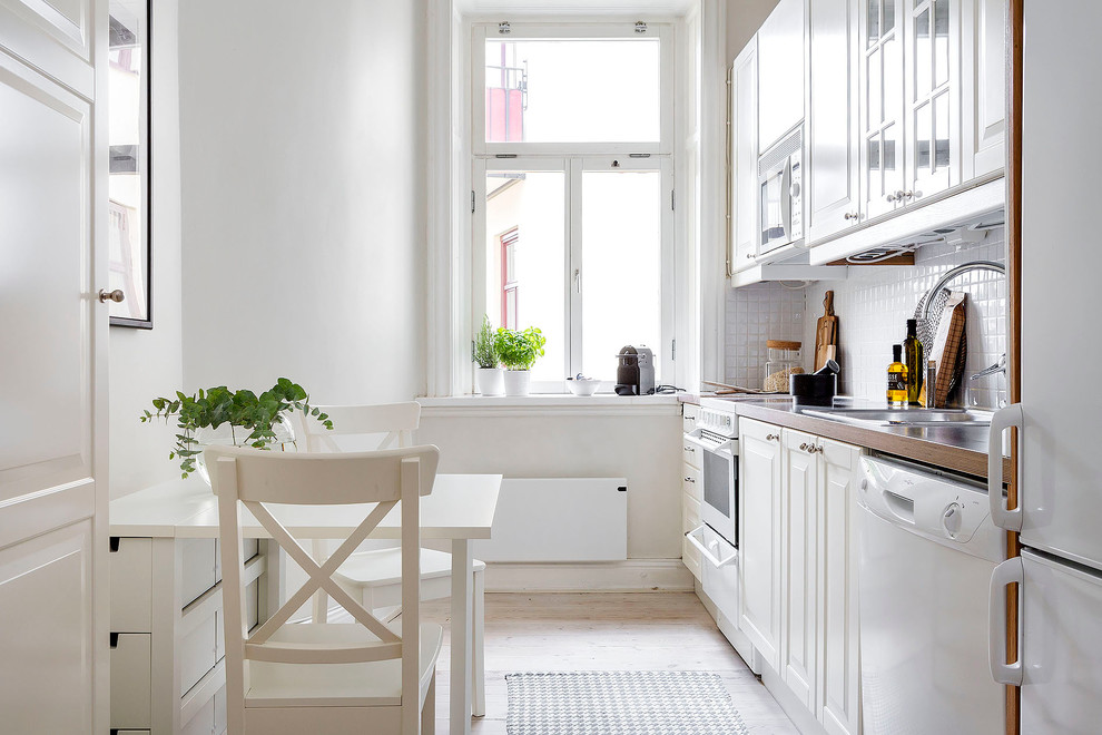 Idéer för att renovera ett mellanstort skandinaviskt linjärt kök och matrum, med en nedsänkt diskho, luckor med upphöjd panel, vita skåp, vitt stänkskydd, vita vitvaror, ljust trägolv, träbänkskiva och stänkskydd i keramik