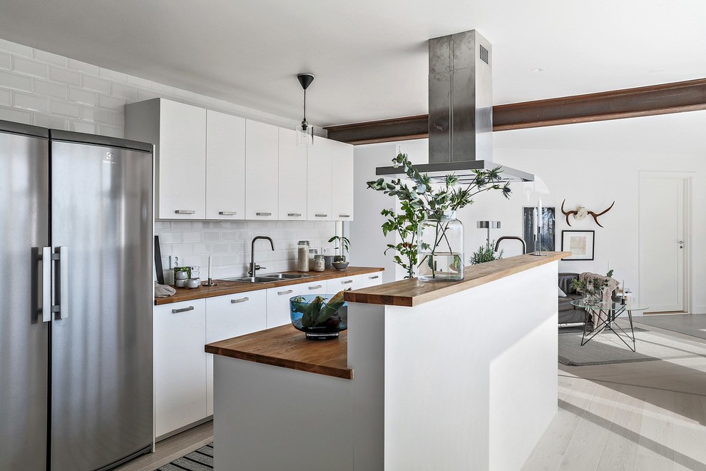 Medium sized scandi galley kitchen/diner in Malmo with wood worktops, light hardwood flooring, an island, white floors, a double-bowl sink, flat-panel cabinets, white cabinets, white splashback, metro tiled splashback, stainless steel appliances and brown worktops.