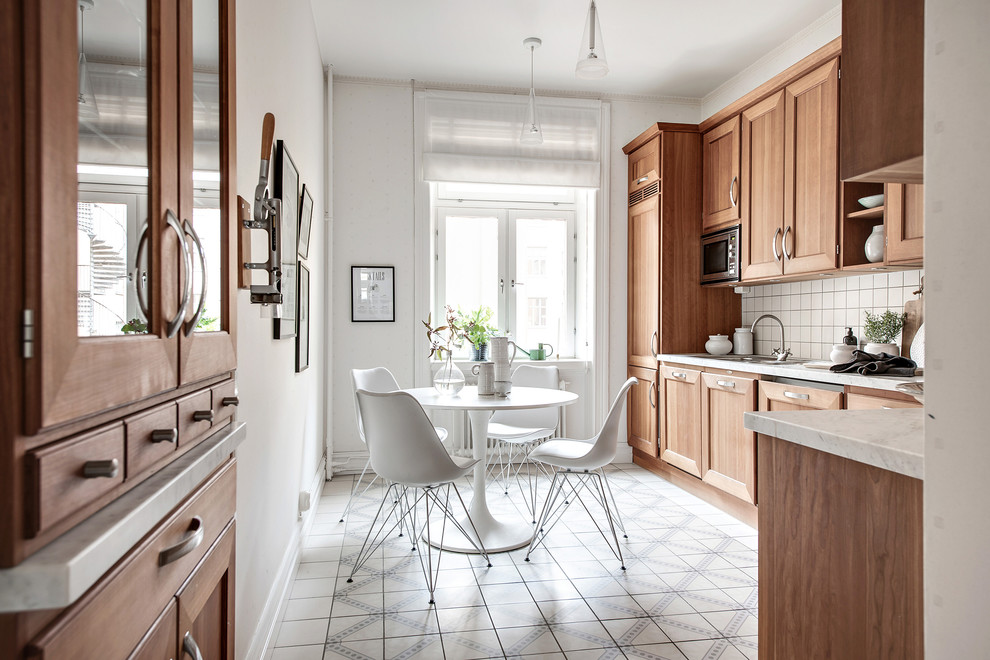 Mittelgroße Skandinavische Wohnküche ohne Insel in L-Form mit Schrankfronten mit vertiefter Füllung, hellbraunen Holzschränken, Granit-Arbeitsplatte, Küchenrückwand in Weiß, Zementfliesen für Boden und buntem Boden in Göteborg
