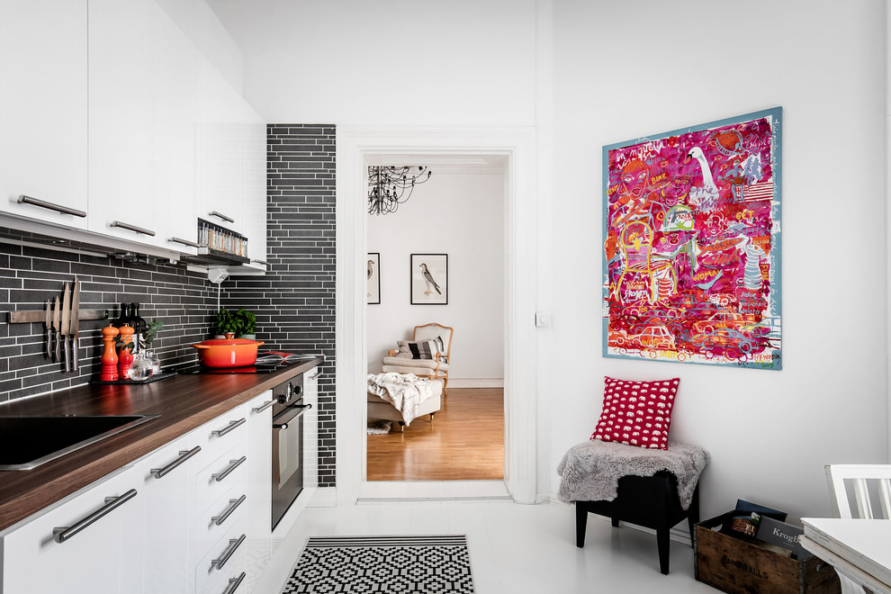 Foto på ett mellanstort minimalistiskt linjärt kök, med en nedsänkt diskho, släta luckor, vita skåp, träbänkskiva, svart stänkskydd, stänkskydd i mosaik, svarta vitvaror och målat trägolv