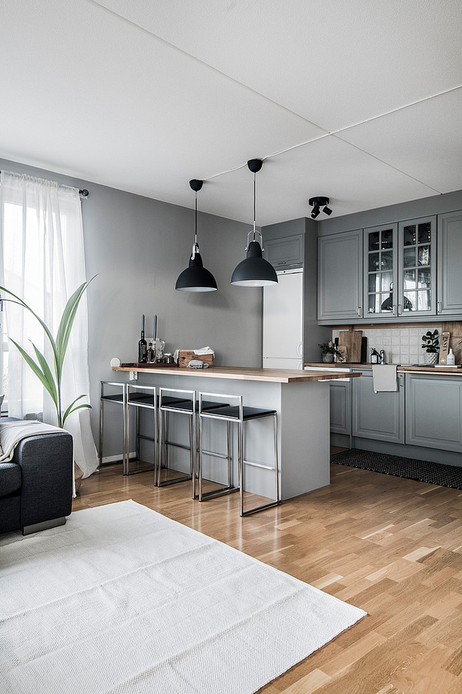 Foto på ett skandinaviskt brun kök, med luckor med upphöjd panel, grå skåp, träbänkskiva, vitt stänkskydd, stänkskydd i keramik, vita vitvaror, mellanmörkt trägolv, en halv köksö och beiget golv