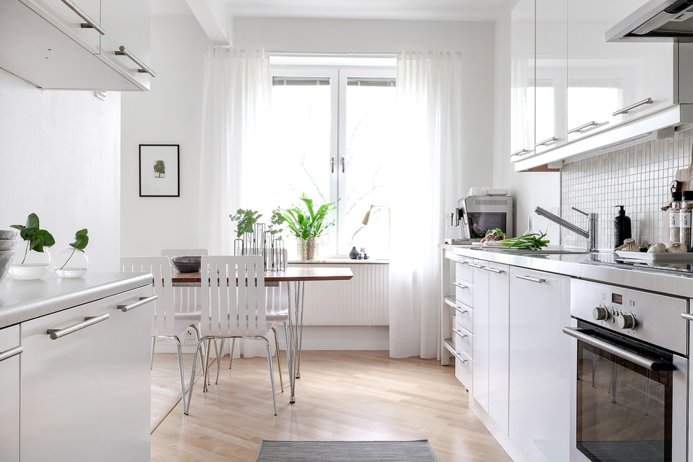 Inspiration for a scandi kitchen/diner in Gothenburg with flat-panel cabinets, white cabinets, white splashback, stainless steel appliances, light hardwood flooring, no island and beige floors.