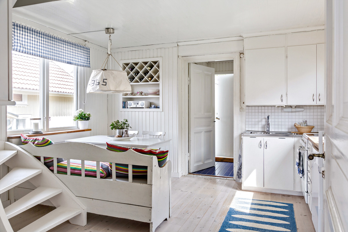 ヨーテボリにある中くらいなビーチスタイルのおしゃれなキッチン (フラットパネル扉のキャビネット、白いキャビネット、白いキッチンパネル、サブウェイタイルのキッチンパネル、淡色無垢フローリング、ベージュの床、アイランドなし) の写真