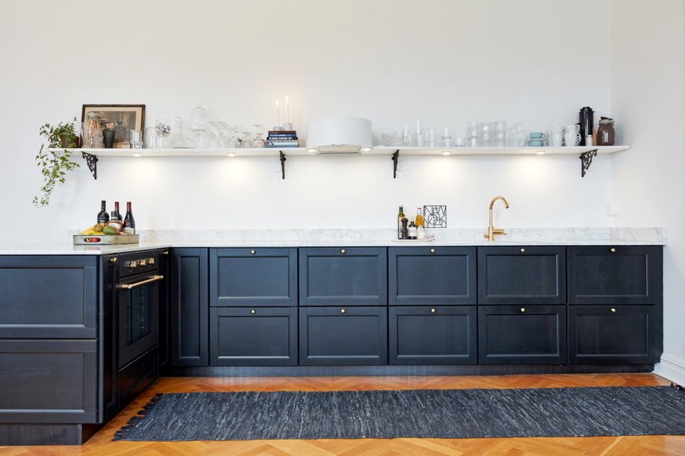 Modelo de cocina lineal clásica de tamaño medio sin isla con armarios con paneles empotrados, puertas de armario azules, encimera de mármol y suelo de madera en tonos medios