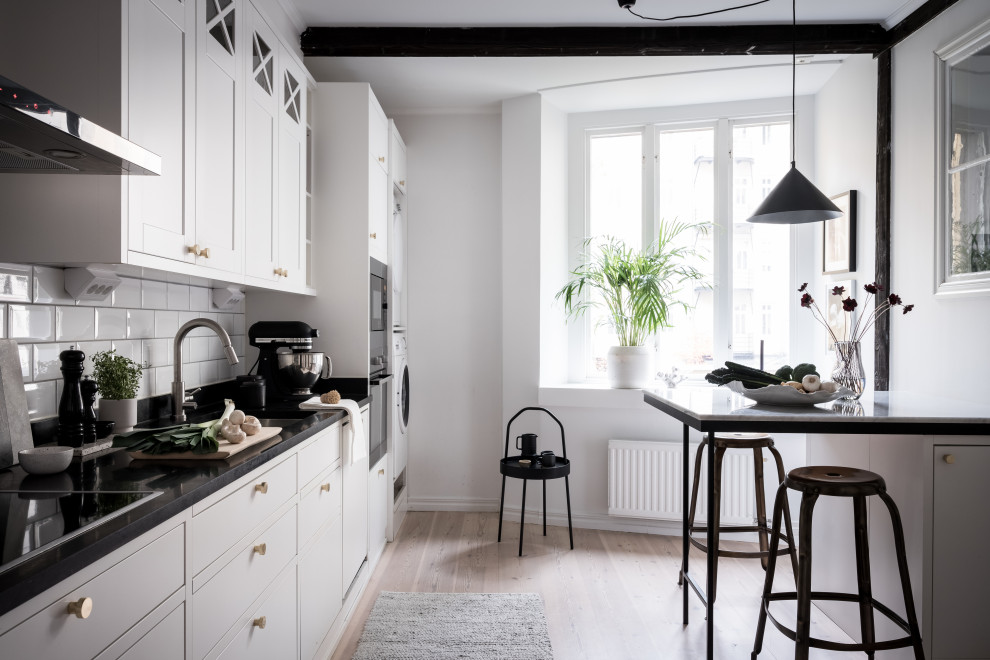 Bild på ett minimalistiskt svart linjärt svart kök, med en undermonterad diskho, släta luckor, vita skåp, vitt stänkskydd, stänkskydd i tunnelbanekakel, rostfria vitvaror och en halv köksö