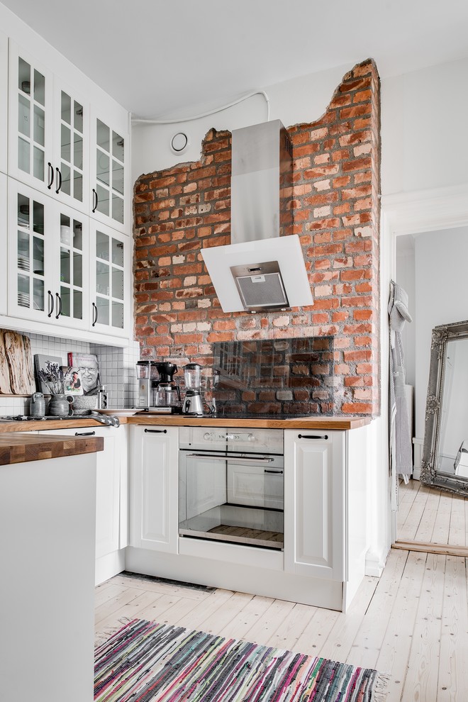 Photo of a small scandinavian u-shaped kitchen in Gothenburg with recessed-panel cabinets, white cabinets, wood worktops, glass sheet splashback, stainless steel appliances, light hardwood flooring and no island.