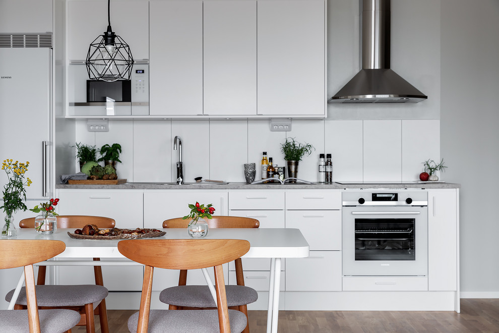 Inspiration för ett skandinaviskt grå linjärt grått kök och matrum, med släta luckor, vita skåp, vita vitvaror, mellanmörkt trägolv och brunt golv